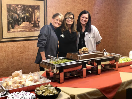 Three people stand together in front of a buffet setup at an event.