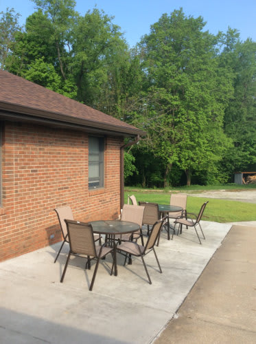 A patio with outdoor furniture next to a brick building surrounded by greenery.