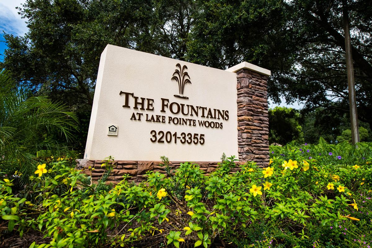 Entrance sign for The Fountains at Lake Pointe Woods surrounded by greenery and flowers.