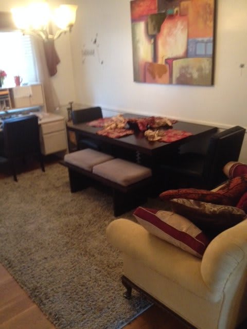 A cozy dining room with a dark wooden table, chairs, and a bench, accented by a plush rug and wall artwork.