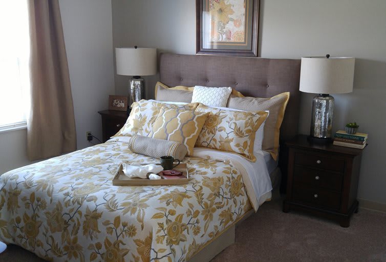 A cozy bedroom featuring a bed with floral bedding and decorative pillows, accompanied by lamps on nightstands.