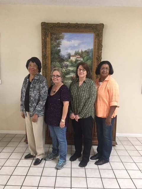 A group of four people standing indoors in front of a framed painting.