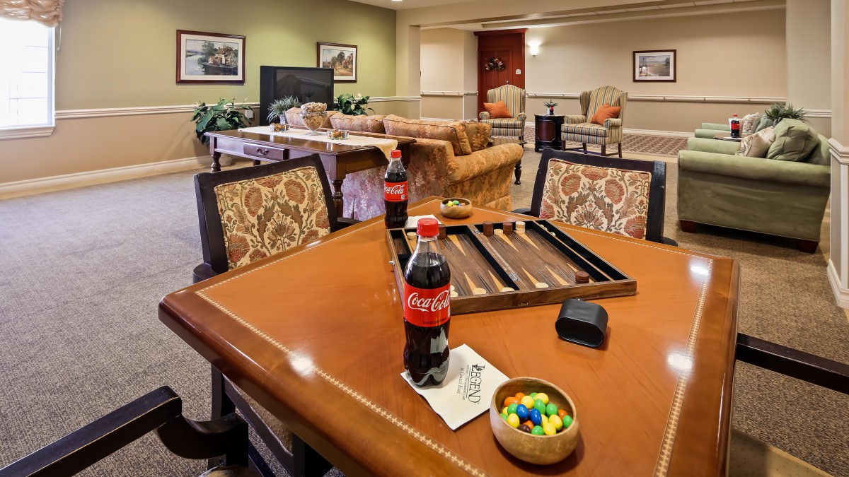 A cozy living room setting with a table set for backgammon, featuring a Coca-Cola bottle and a bowl of M&Ms.