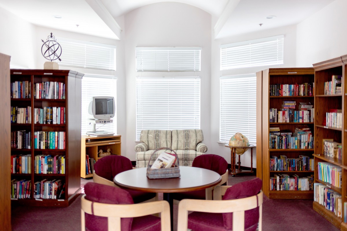 A cozy library with a round table and chairs, surrounded by bookshelves and a sofa.