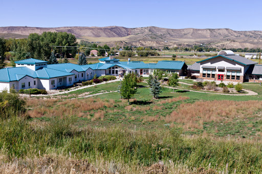 Aerial view of a complex with blue roofs surrounded by grassy fields and mountains in the background.