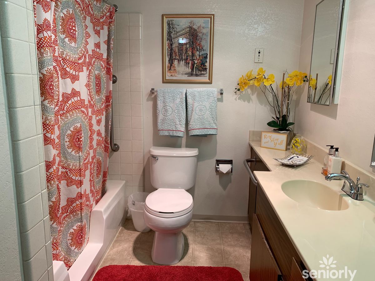 A neatly organized bathroom with a red and white shower curtain, a toilet, and a countertop with flowers and decorative items.