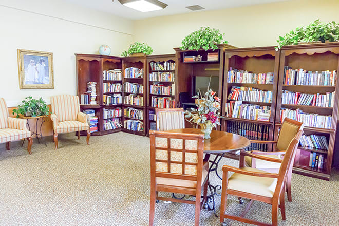 A cozy library room with bookshelves, chairs, and a table for reading.