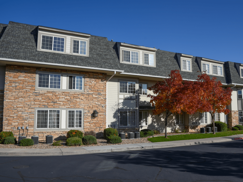 A residential apartment building with a brick exterior, surrounded by autumn foliage under a clear blue sky.