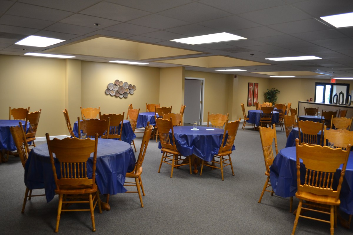 An empty banquet hall with tables and chairs arranged, covered with blue tablecloths.