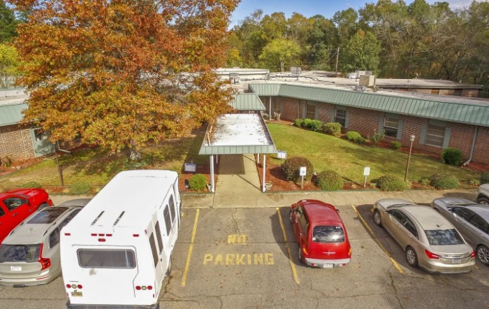A building with a covered entrance, surrounded by autumn trees, and a parking lot marked 'No Parking'.