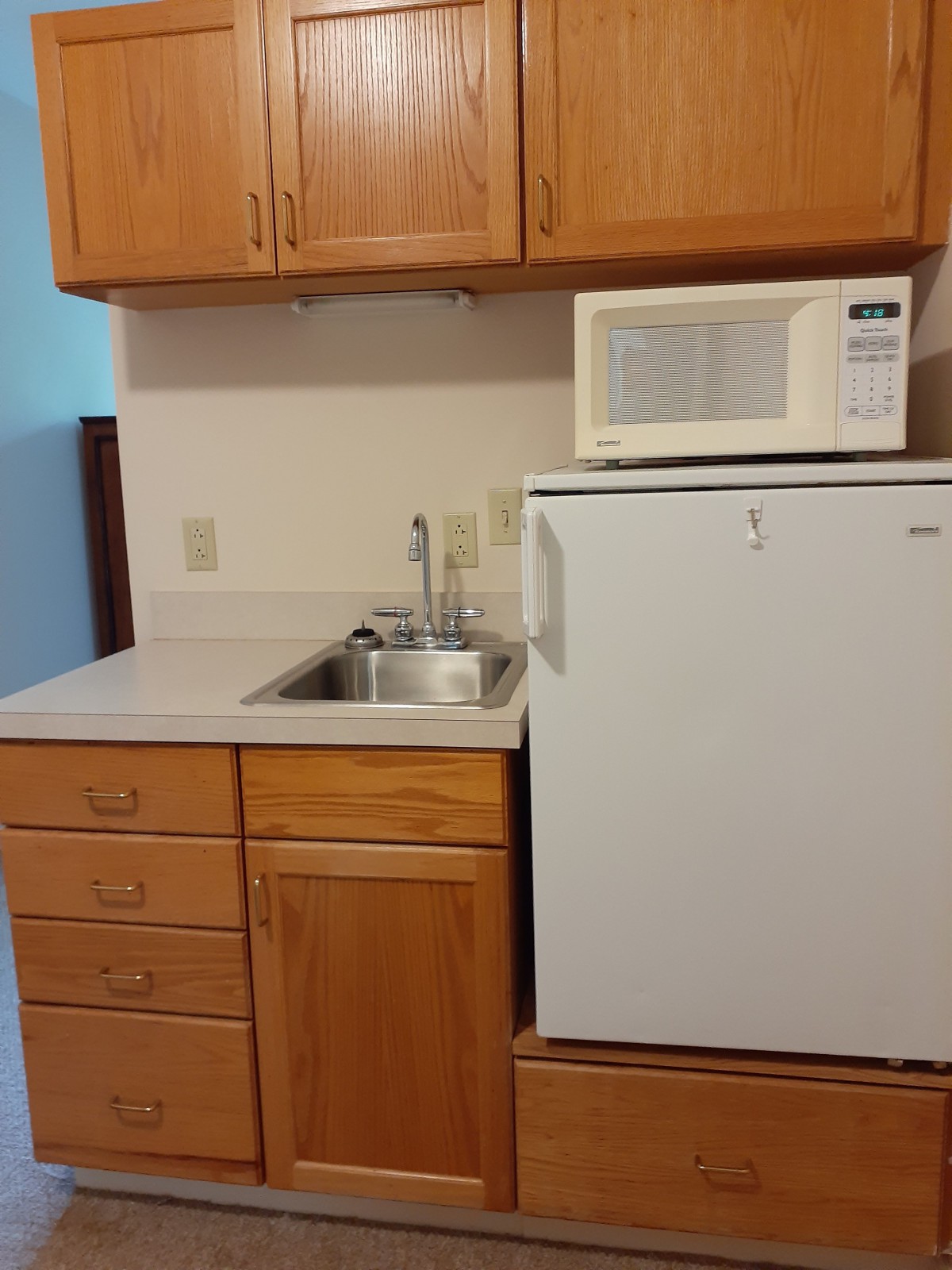 A compact kitchen area with a sink, microwave, and small fridge.