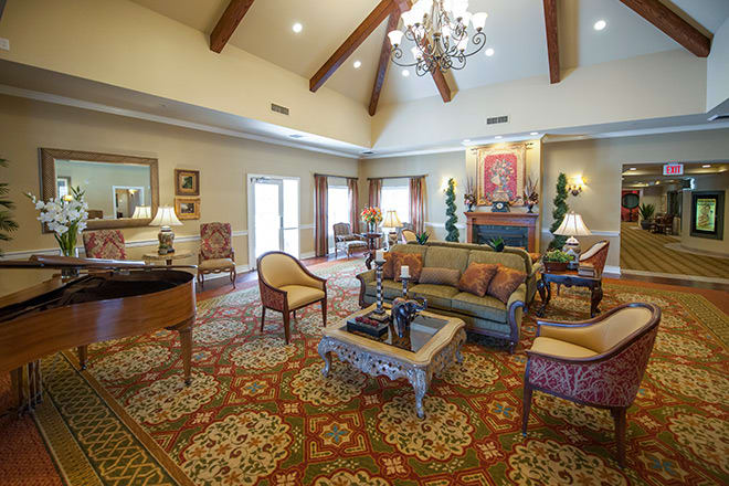 A spacious and elegantly decorated living room with a high ceiling, featuring a chandelier, comfortable seating arrangements, and warm lighting.