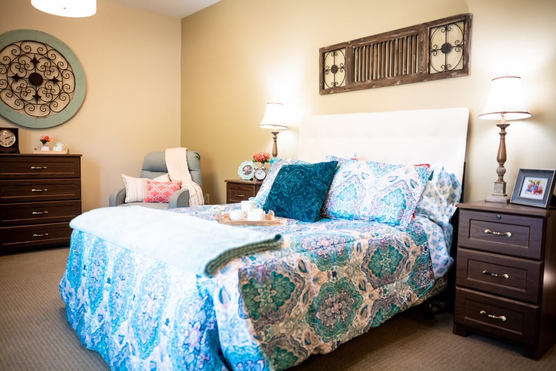 A cozy bedroom featuring a colorful bedspread, pillows, and a bedside lamp.