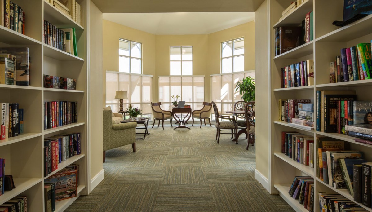 A cozy library reading area with comfortable chairs, large windows, and bookshelves.