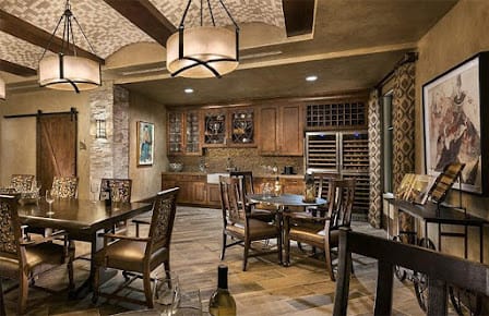 A rustic wine cellar with wood furniture and brick walls, featuring cozy lighting and well-stocked shelves.