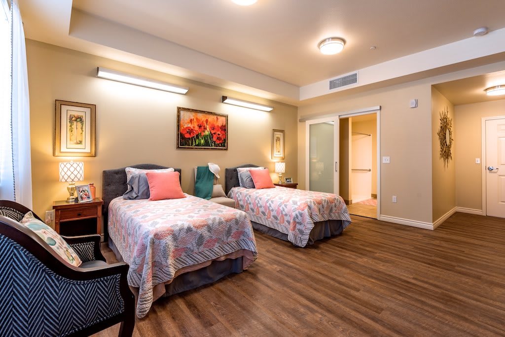 A cozy bedroom featuring twin beds with floral bedspreads, soft lighting, and hardwood floors.