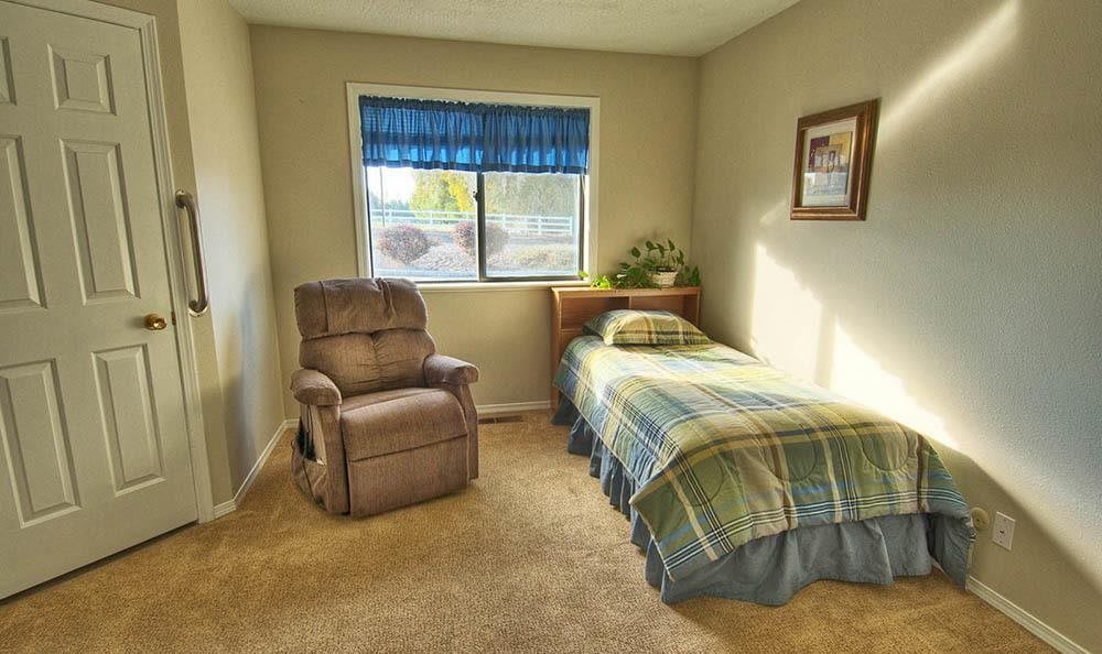 A cozy bedroom with a single bed and a recliner chair by the window.
