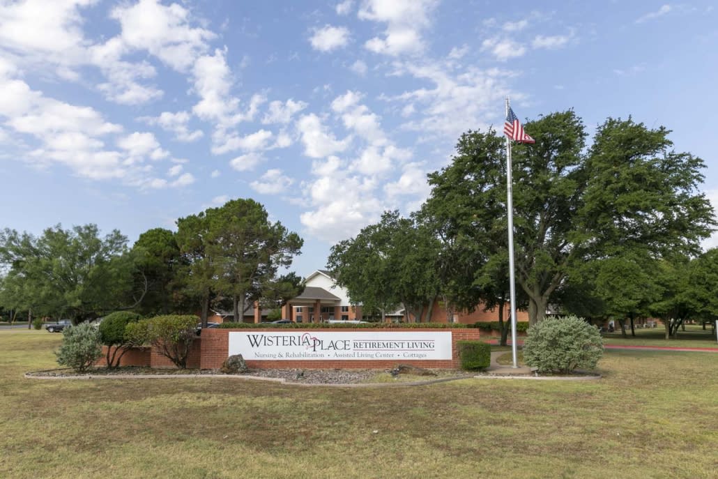 A view of a school entrance featuring a sign, trees, and an American flag on a flagpole.