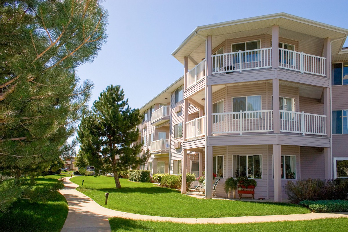 A sunny day view of a residential apartment building with balconies and surrounding greenery.