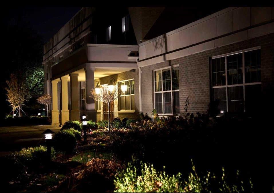 A well-lit building entrance at night surrounded by landscaping.