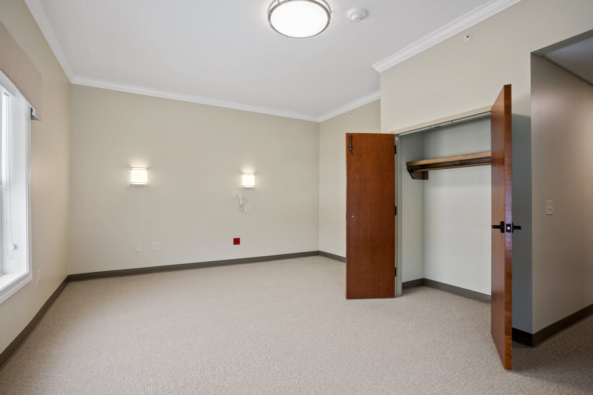 A vacant room with neutral-colored walls, two wall-mounted light fixtures, and an open closet.