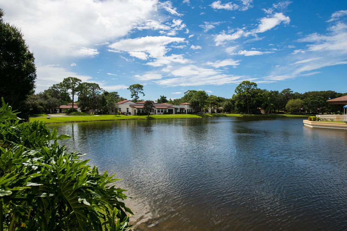 A tranquil lakeside view with houses and lush greenery under a vibrant blue sky.