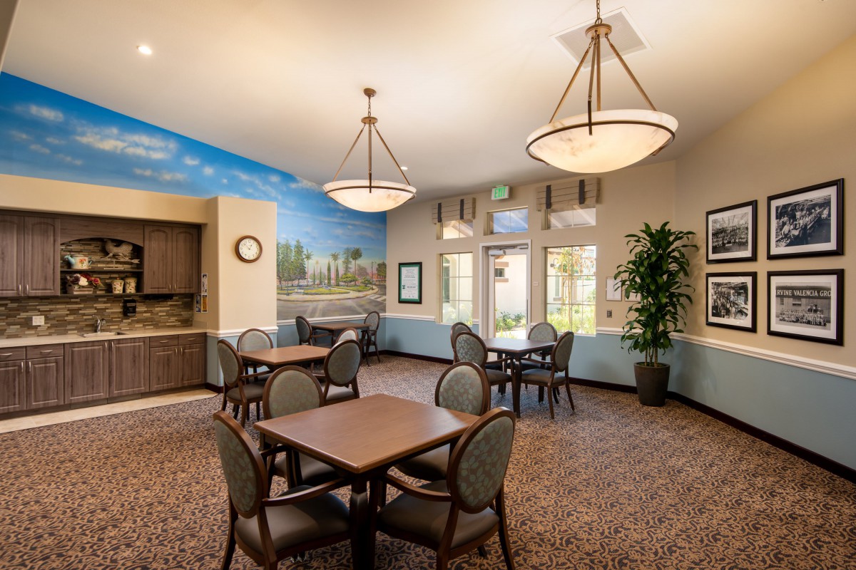 A well-lit dining area featuring multiple tables and chairs, with decorative elements such as a mural and indoor plants.