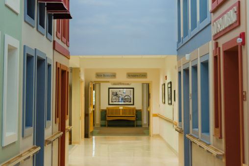 A serene and spacious hallway featuring a waiting area with a bench, framed artwork, and soft lighting.