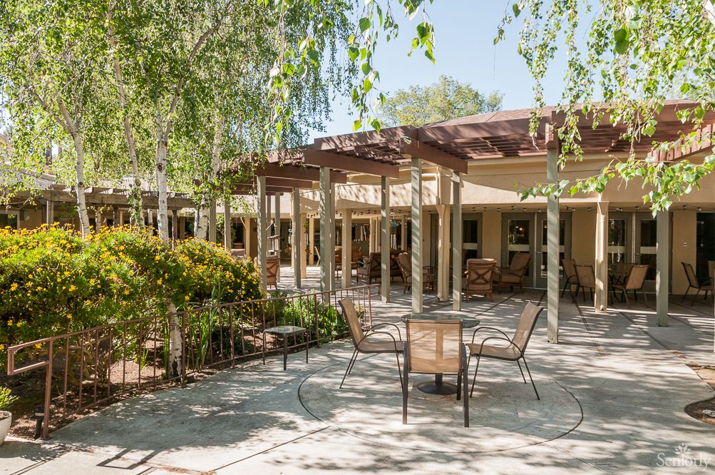 A tranquil outdoor patio area with tables, chairs, and a pergola amidst lush greenery.