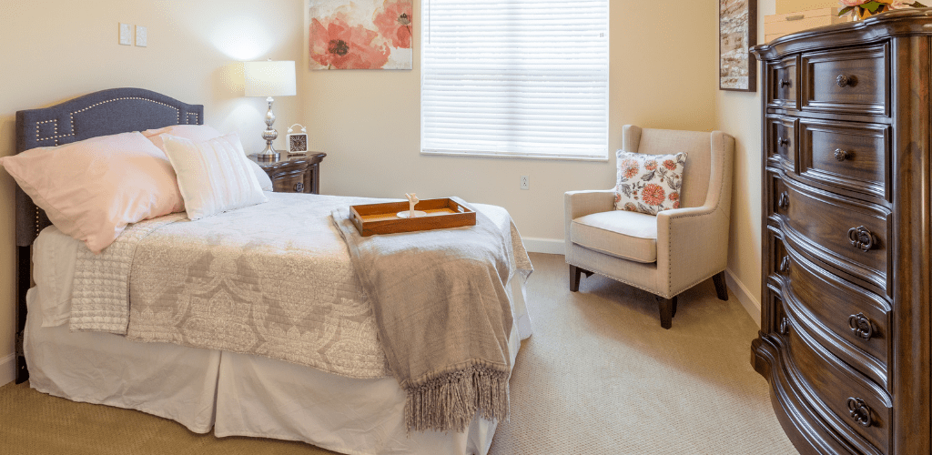 A cozy bedroom with a neatly made bed, an armchair, and soft lighting.