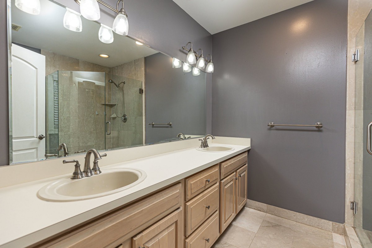 A modern bathroom with a large mirror, dual sinks, and a spacious shower area.