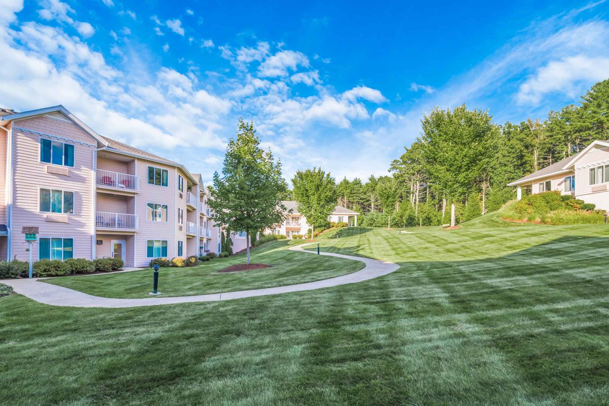 A scenic view of apartment buildings with a well-maintained green lawn and pathway under a partly cloudy sky.