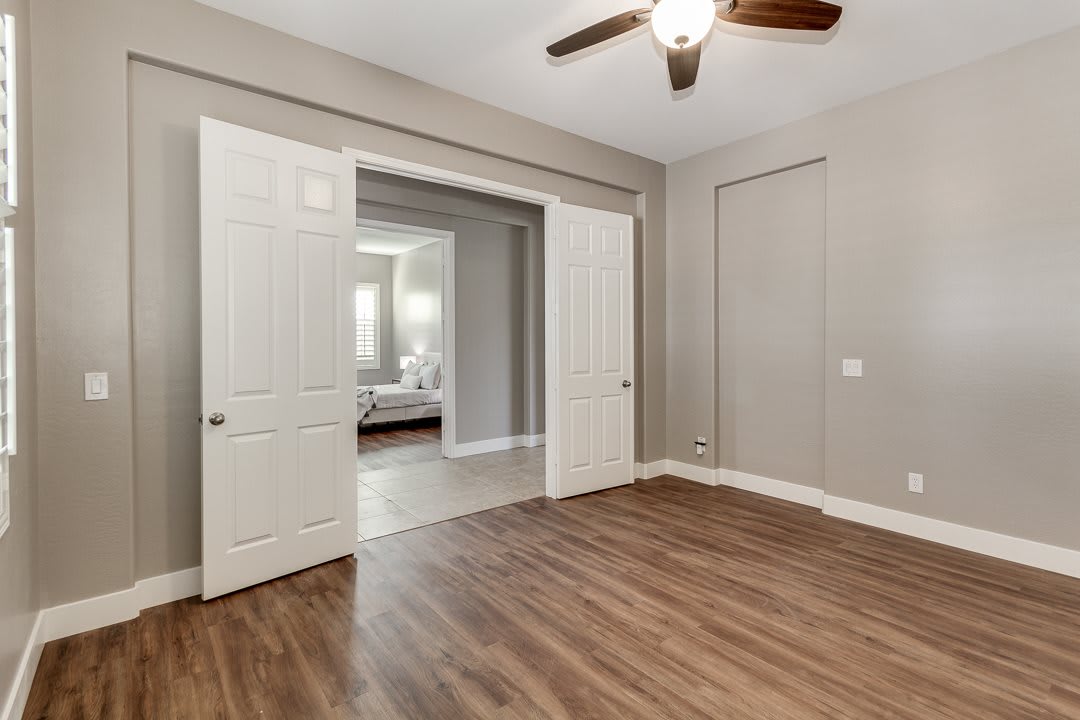 An empty room with hardwood flooring, a ceiling fan, and an open doorway leading to another space.