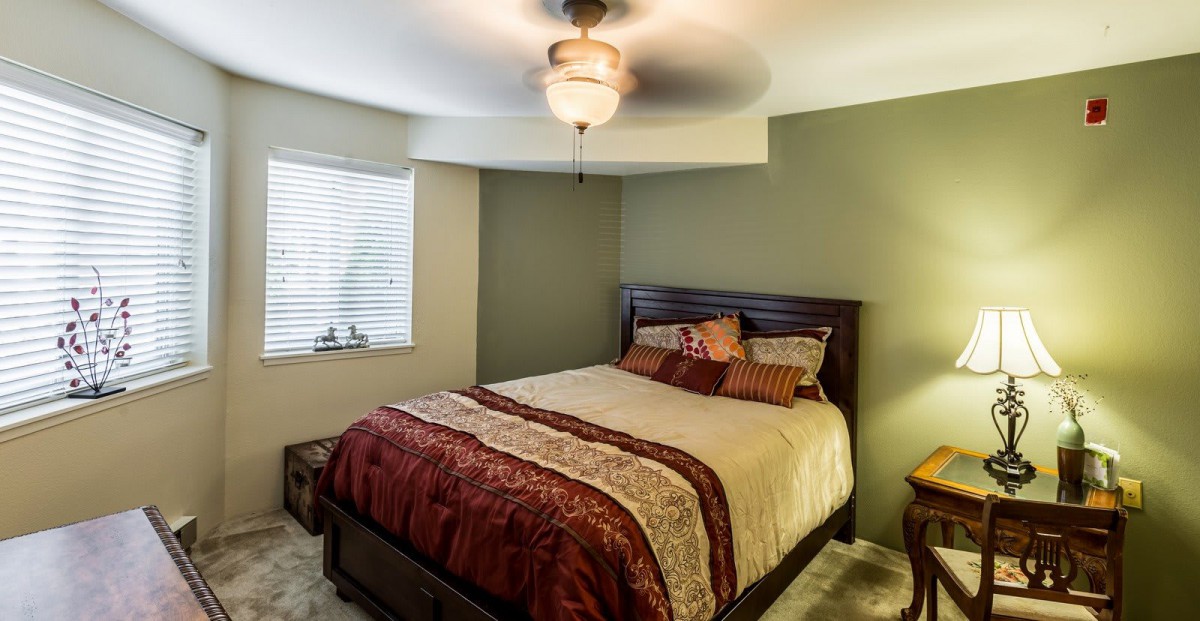 A cozy bedroom featuring a neatly made bed with decorative pillows and a ceiling fan.