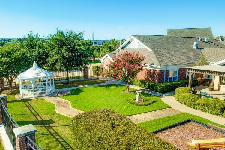 A quaint building surrounded by a well-manicured lawn and garden, featuring a charming gazebo.