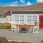 A cozy patio with two white rocking chairs and an American flag in front of a building with a red door.
