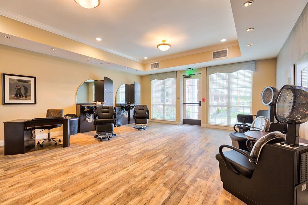 An empty hair salon with modern furnishings, including chairs and mirrors, set against a backdrop of large windows and bright lighting.