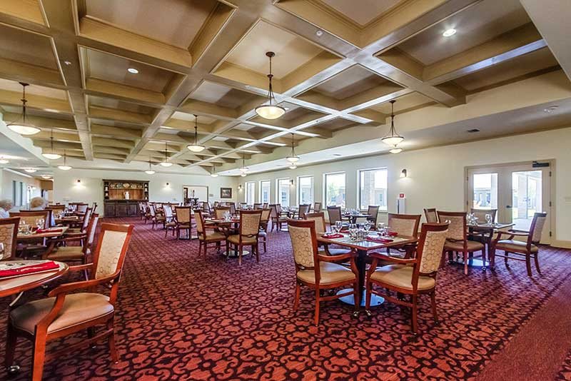 An elegant dining room with tables and chairs, featuring ceiling lights and large windows.