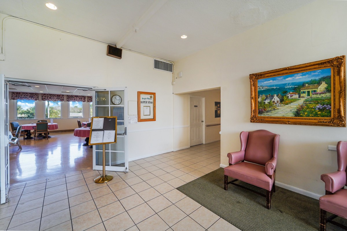 A lobby area featuring a pink armchair, a framed painting on the wall, and tiled flooring.