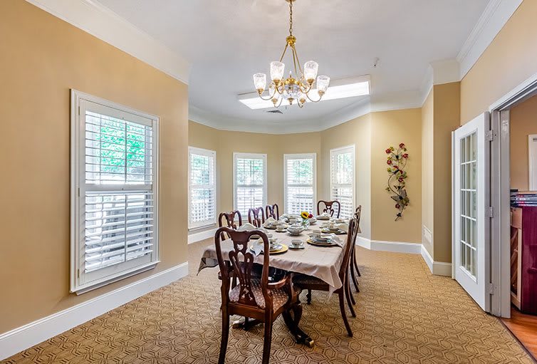 An elegant dining room with a large table, chairs, and a chandelier, surrounded by multiple windows.