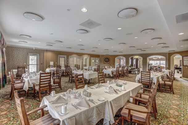 An elegantly set dining room with tables and chairs arranged neatly, featuring white tablecloths.