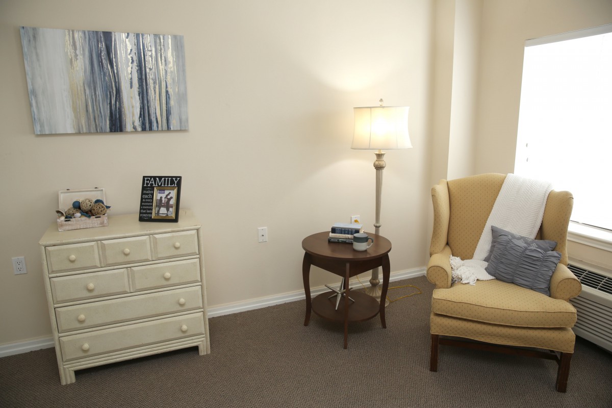 A cozy living room corner with a yellow armchair, side table, and lamp alongside a white dresser.