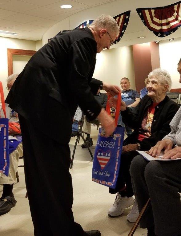 An elderly woman receives a gift bag from a man during an indoor gathering.