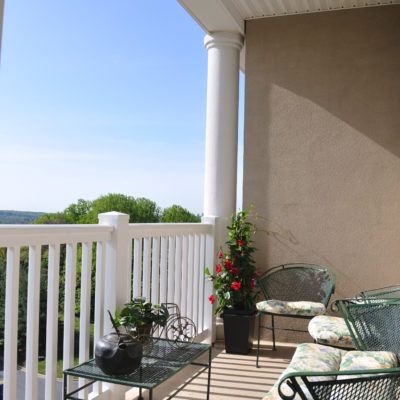 A sunny balcony with outdoor seating and potted plants.