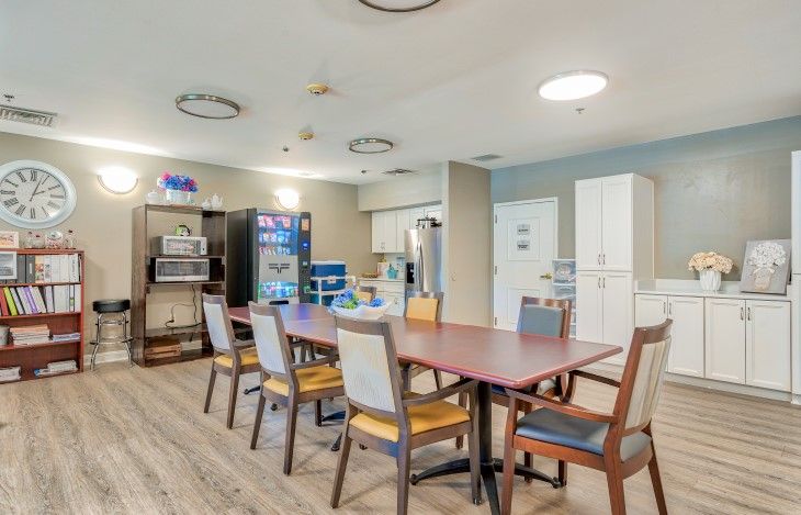 A communal dining area with a large table, chairs, vending machine, and storage cabinets.