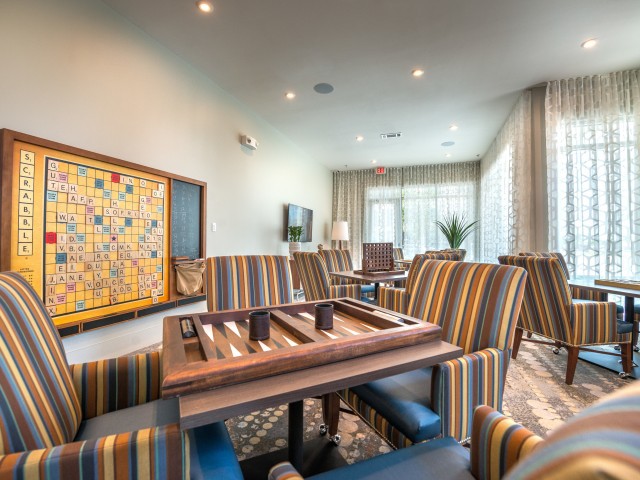 A modern living room featuring a backgammon board on a table surrounded by striped chairs.