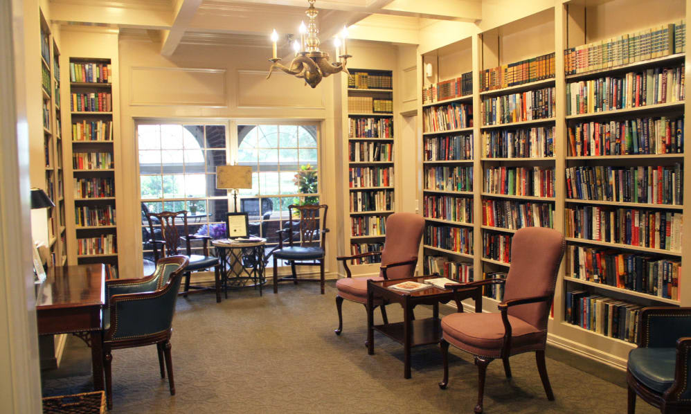A cozy library reading room with bookshelves, comfortable chairs, and large windows.