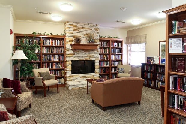 A cozy library room with bookshelves, a stone fireplace, and comfortable seating.