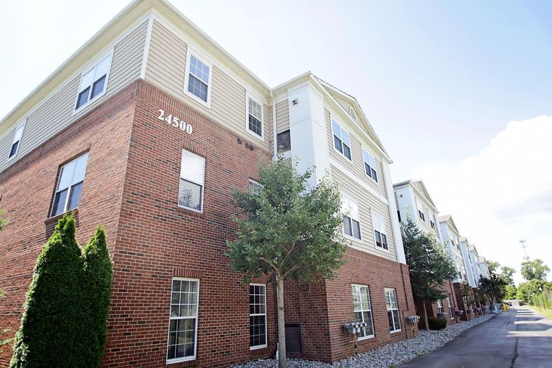A three-story apartment building with a brick facade and a tree in front.