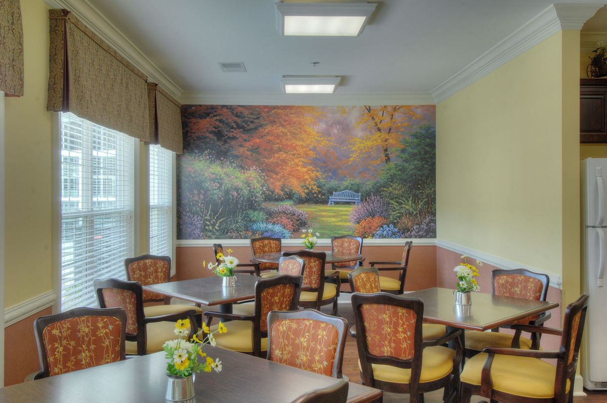 A cozy dining room with tables and chairs, adorned with a large mural of an autumn landscape.